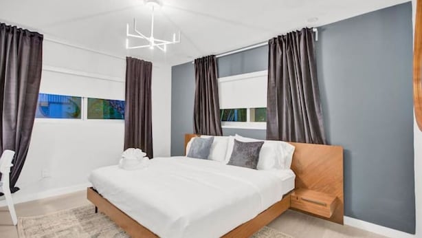 Une chambre moderne avec un cadre de lit en bois, une literie blanche et une grande fenêtre avec des rideaux.