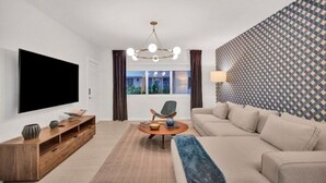 Un salon moderne avec un téléviseur à écran plat, un meuble de rangement en bois, une table basse ronde, un canapé beige et un mur décoré d’un motif.