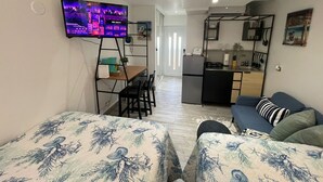 A compact living space with a TV mounted on the wall, a kitchenette, a dining area, and a sofa with patterned bedding. - Charming Isla Verde Studio (Carolina)