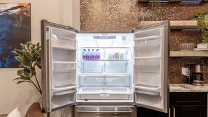 Frigorifero aperto con bottiglie d'acqua e snack, una pianta e un bancone della cucina con una macchina per il caffè.