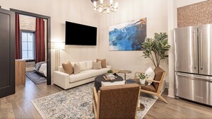 Un soggiorno moderno con un divano bianco, un tavolino, una TV a parete e un frigorifero in acciaio inossidabile.