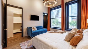 Ett modernt sovrum med en stor säng, en blå soffa, en tv och utsikt över staden.