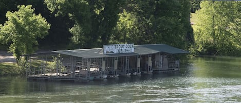 En fortøjet båd med en overdækket struktur, et skilt der siger "Anglers Trout Dock", og et telefonnummer.