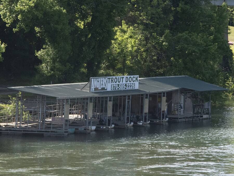 Een vastgemaakt bootje met een overdekte constructie, een bord waarop 'Anglers Trout Dock' staat en een telefoonnummer.