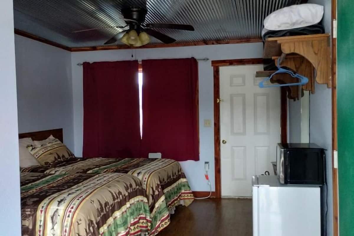 A bedroom with a bed, a ceiling fan, a red curtain, a white door, and a small white refrigerator.