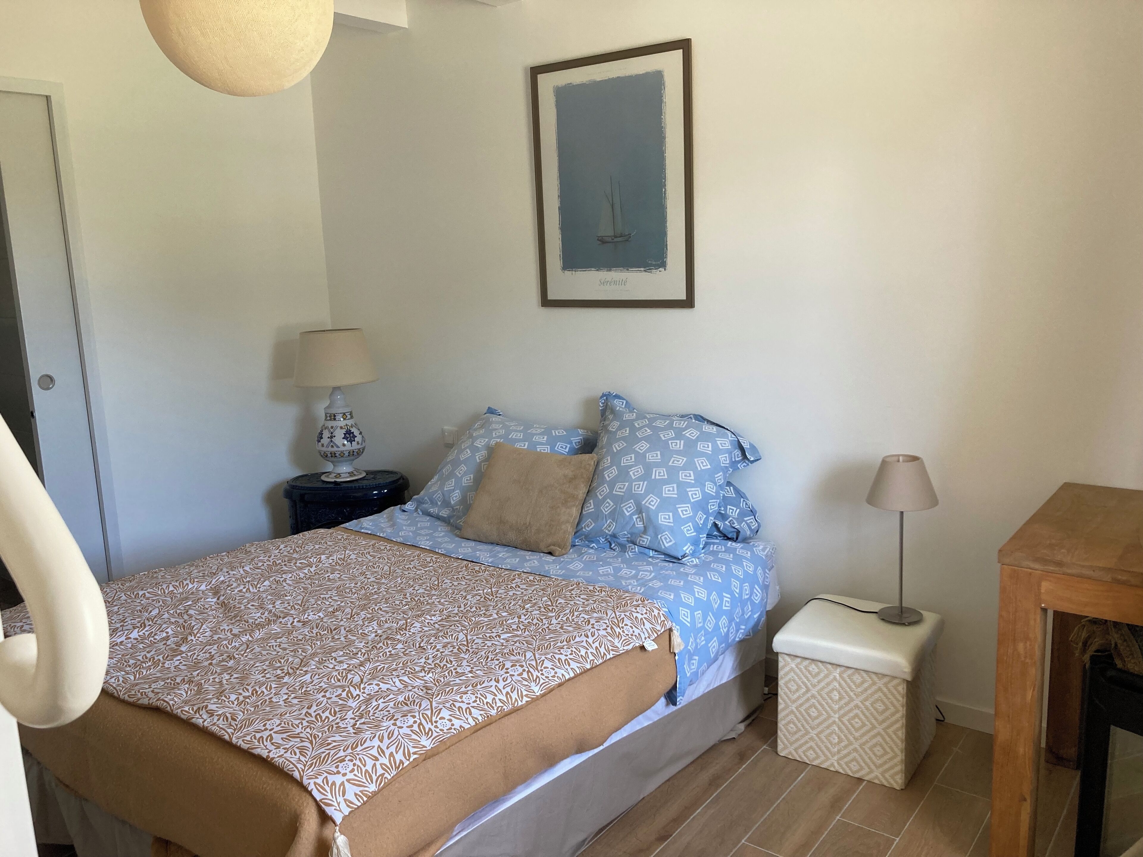 Un dormitorio ordenado con cama, mesita de noche, lámpara y un cuadro en la pared.