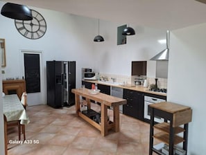 Een compacte keuken met een eethoek, met een houten tafel, een zwarte koelkast, een magnetron en een klok aan de muur.