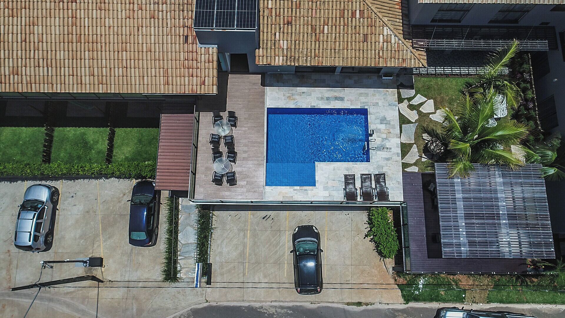 An aerial view of a residential property with a swimming pool, a covered patio, and a parking area.