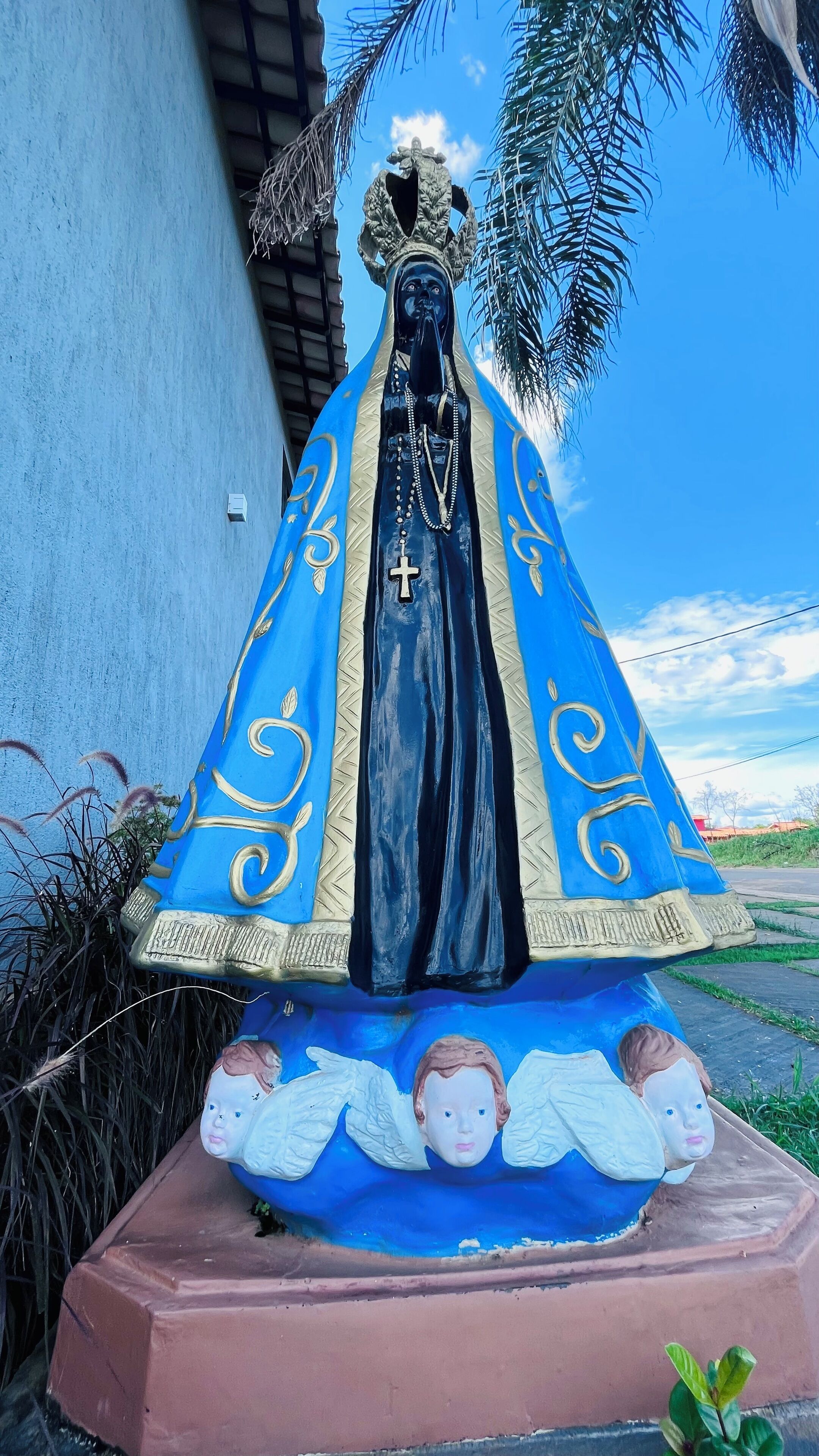A statue of a religious figure with a blue robe and gold trim, standing on a pink base with angelic figures at the feet.