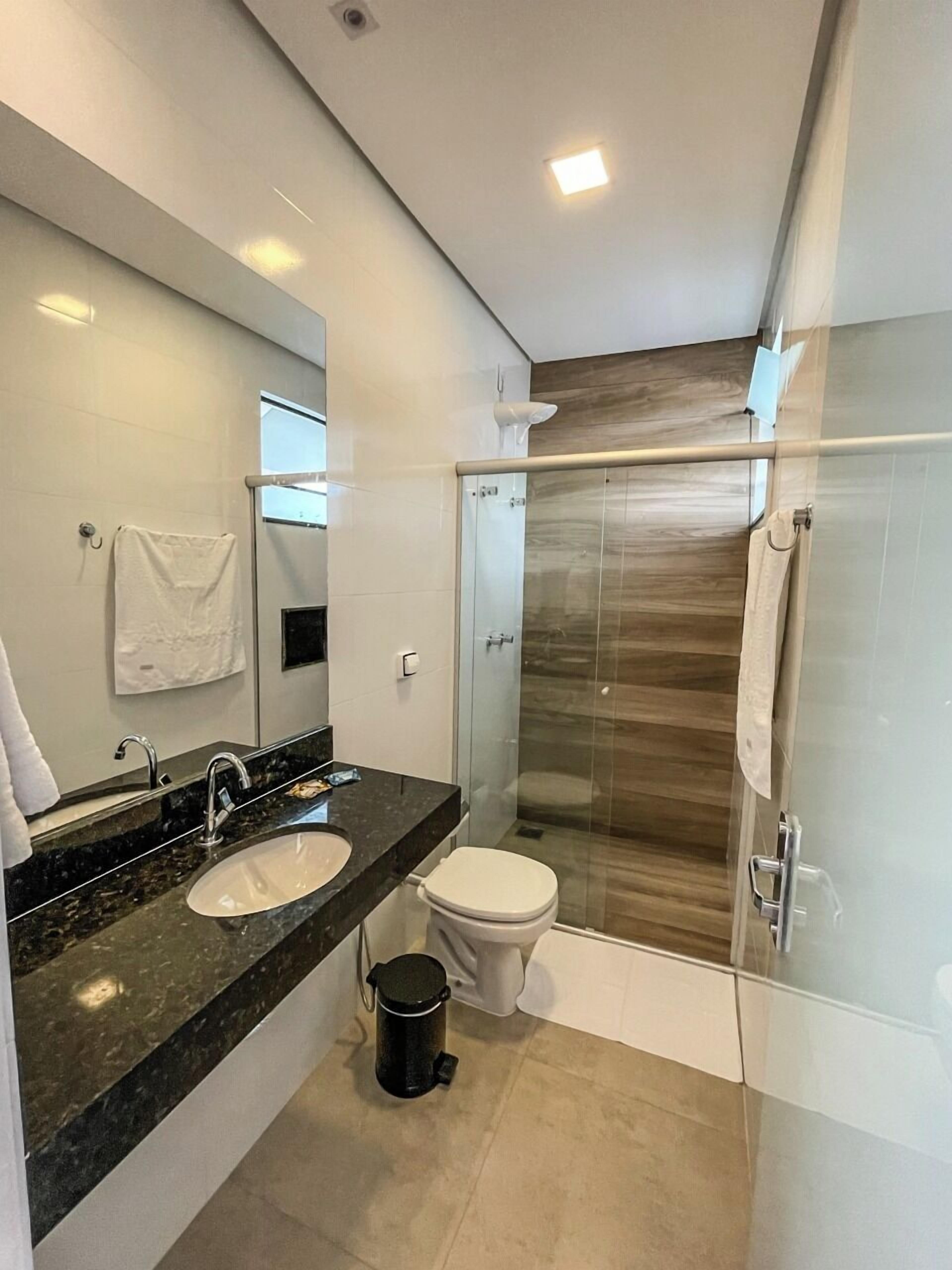 A modern bathroom with a glass shower enclosure, a sink with a marble countertop, and a toilet.