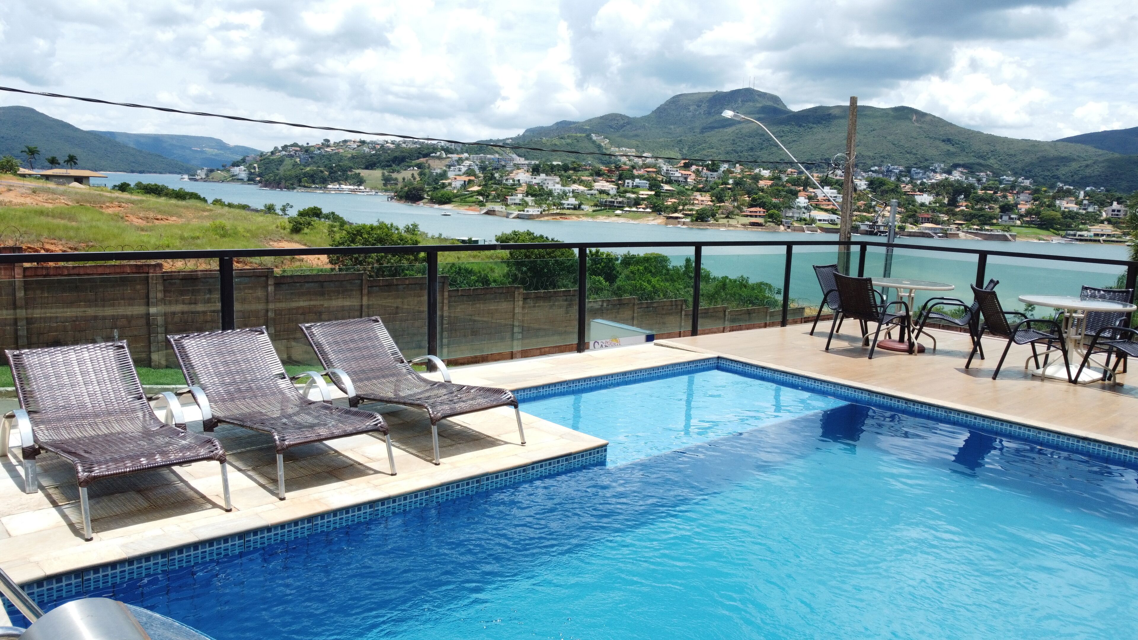 Piscina con sillas de descanso y una mesa, con vistas a un lago y colinas.