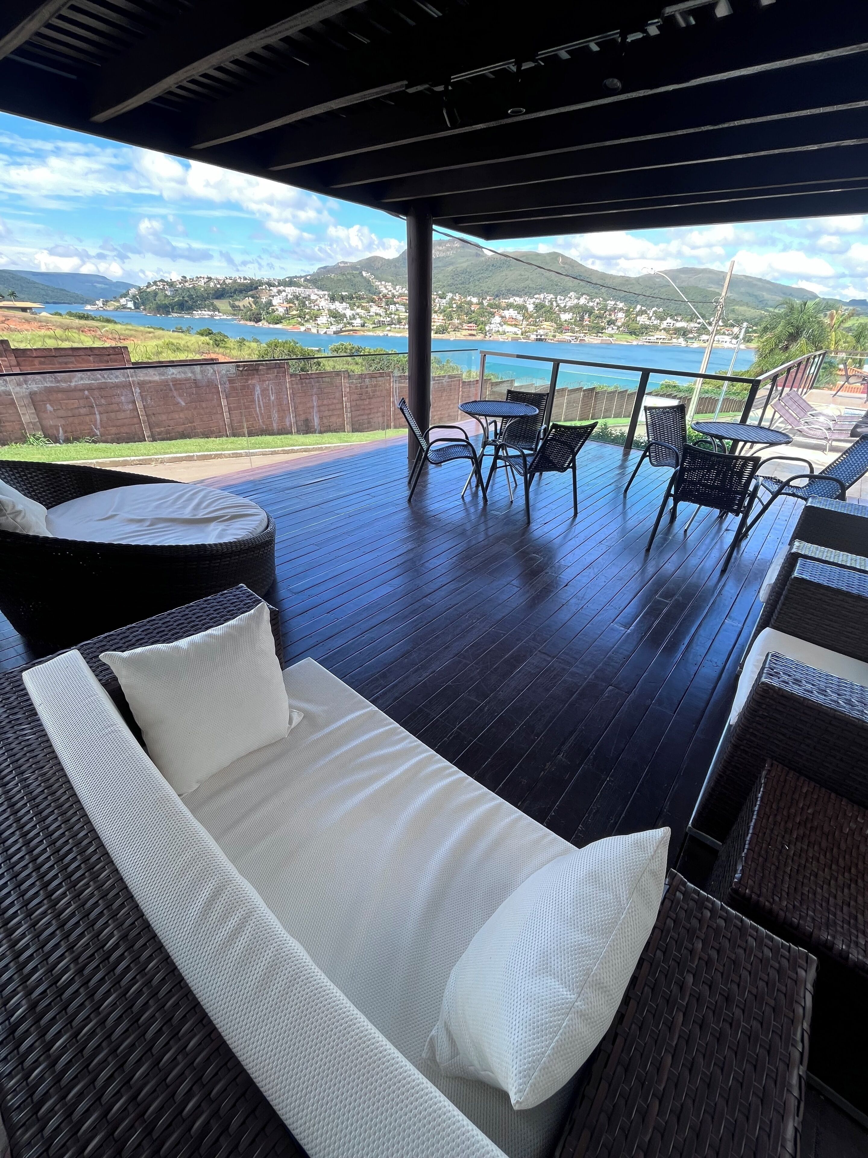 En udendørs terrasse med en fletsofa og stole, med udsigt over et naturskønt sø- og bjerglandskab.