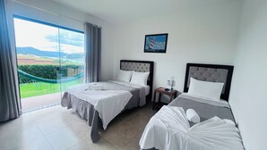 Habitación de hotel con dos camas, vista a un paisaje a través de un ventanal grande y una hamaca afuera.
