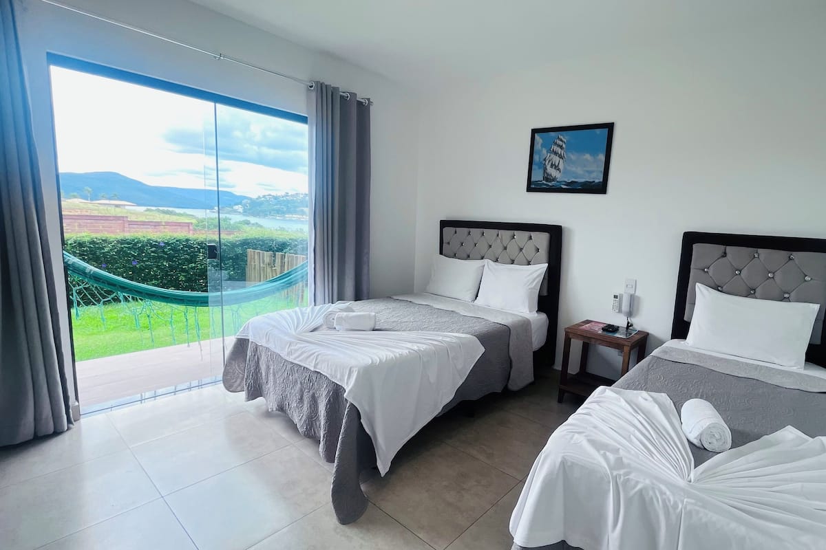 Une chambre d’hôtel avec deux lits, une vue sur un paysage à travers une grande fenêtre et un hamac à l’extérieur.