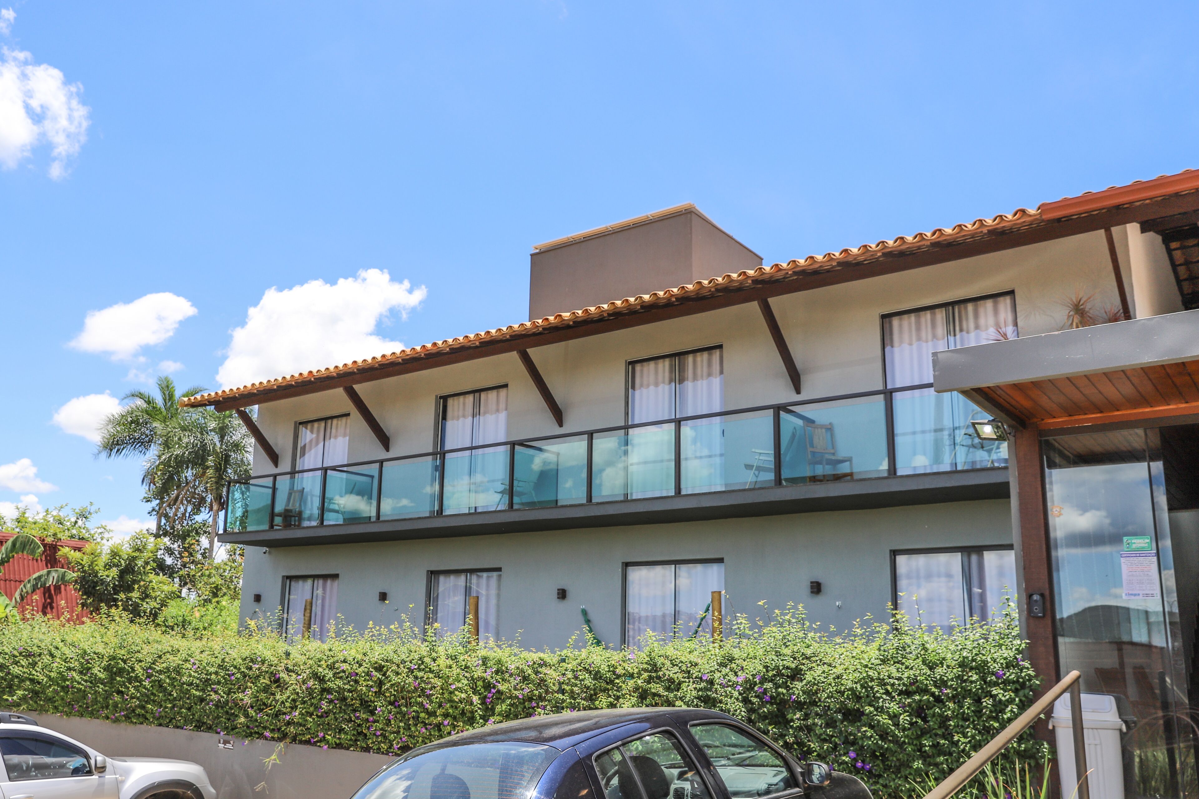 A two-story building with a balcony, a car parked in front, and a clear blue sky.