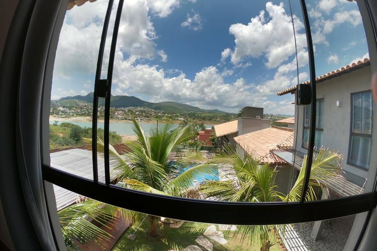 Une vue à travers une fenêtre donnant sur une piscine, des palmiers et une ville lointaine.