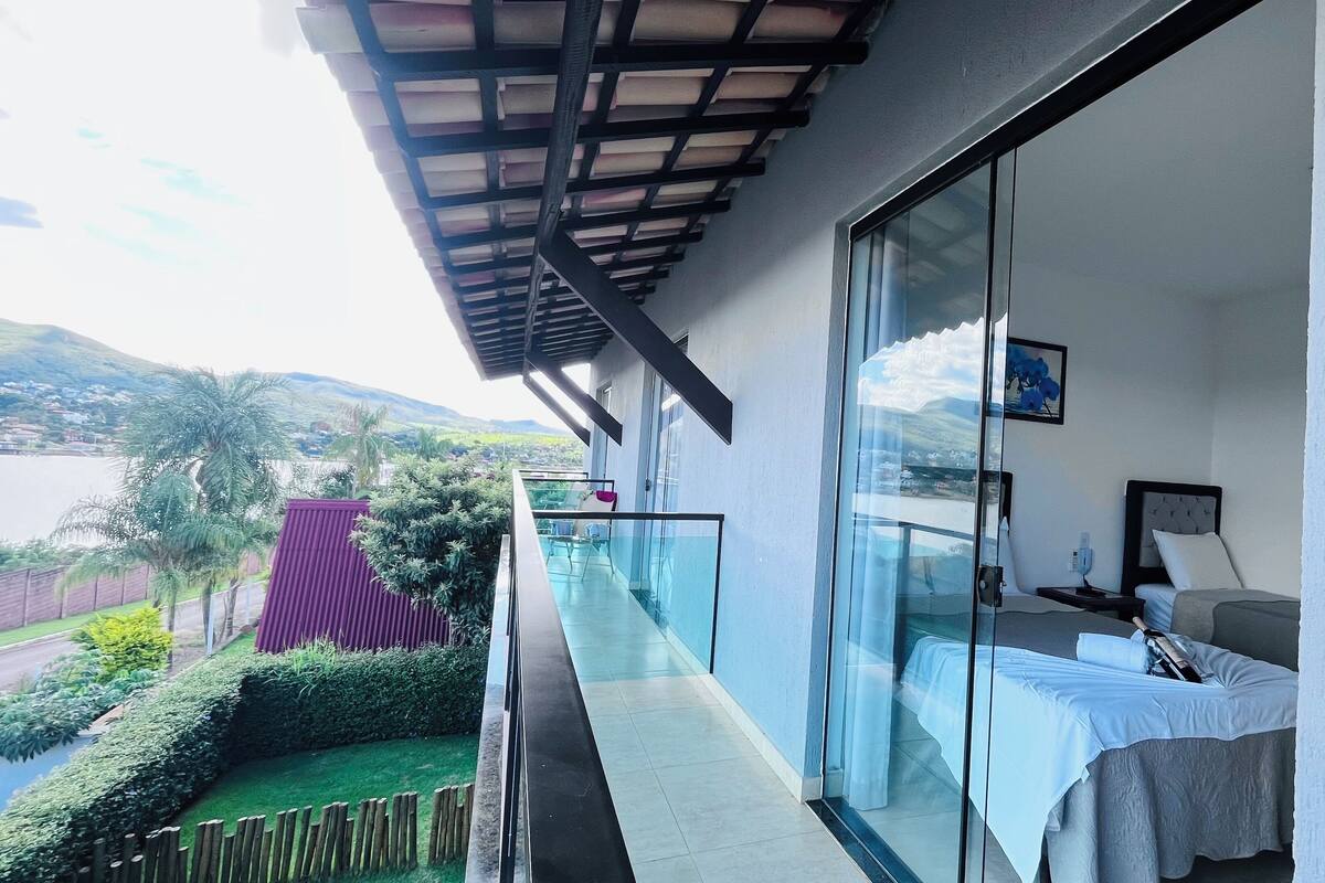 Un balcon avec une barrière en verre, un lit, une table de chevet et un tableau.