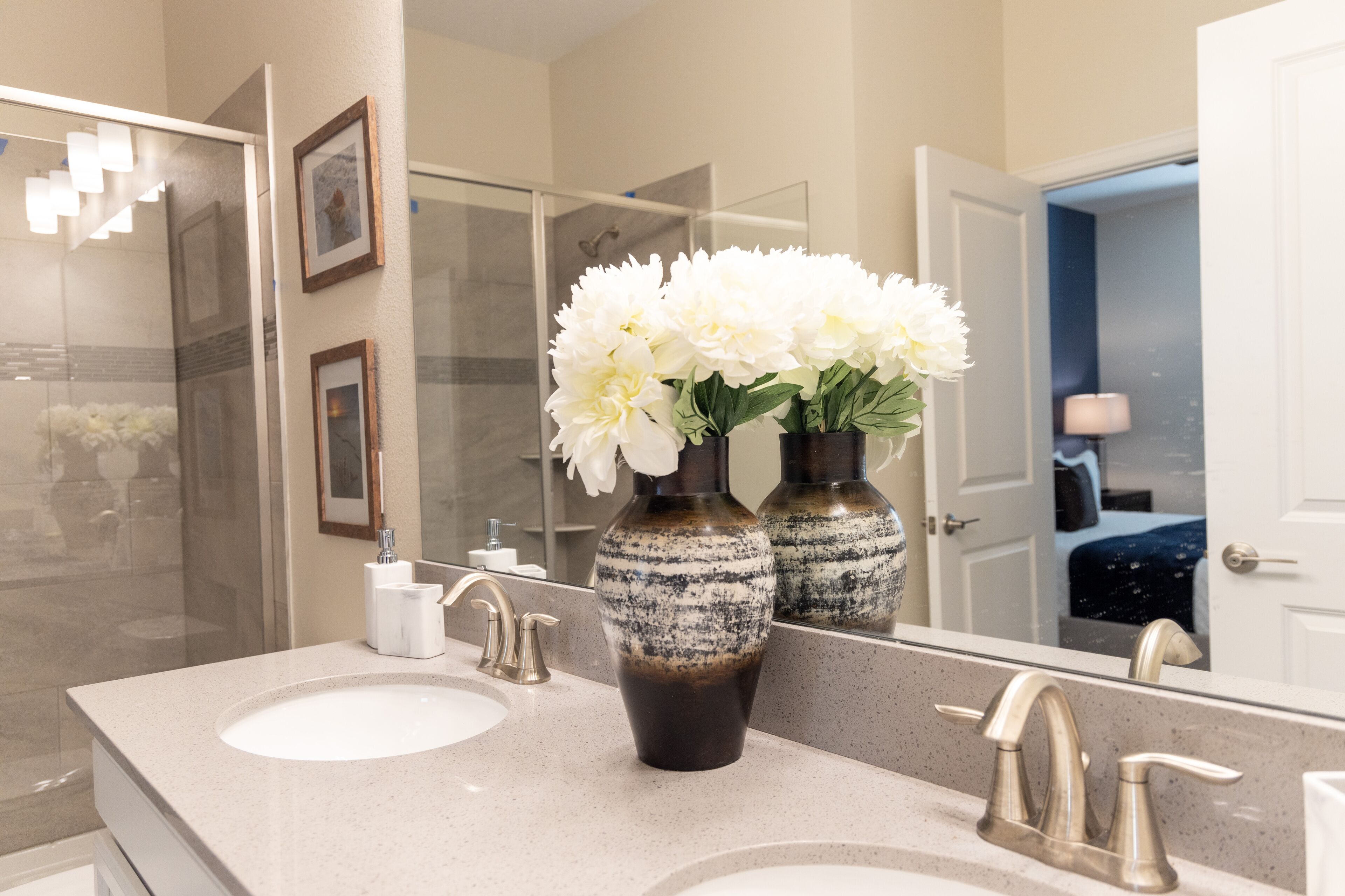 A bathroom with two sinks, a mirror, and a vase with white flowers.