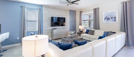 A modern living room with a white sofa, a TV, and a ceiling fan.