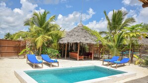 Un espace piscine avec des chaises longues et une structure dotée d’un toit de chaume.