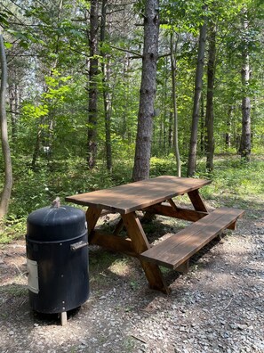 Une table de pique-nique avec des bancs, située dans une zone boisée.