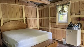 Ein Zimmer mit Holzboden, einem Bett, einem kleinen Schrank und einem Fenster mit Vorhängen.
