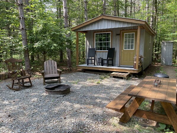 Un chalet rustique doté d’une véranda, de deux fauteuils à bascule, d’un foyer et d’une table de pique-nique.