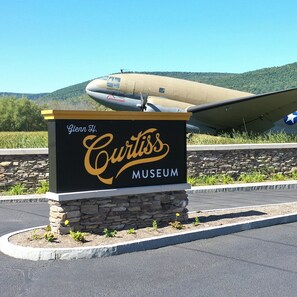 A sign for the Curtiss Museum with a vintage aircraft in the background.