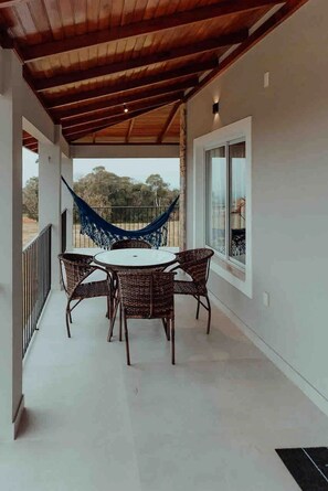 A covered balcony with a table and chairs, a hammock, and a view of the outdoors. - Casa Paraíso do Sol - Rancho Queimado (Rancho Queimado)