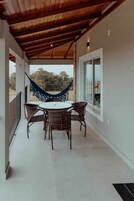 Varanda coberta com mesa e cadeiras, uma rede e vista para o exterior.
