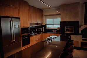 A modern kitchen with wooden cabinets, stainless steel appliances, and a large window providing natural light. - Casa Paraíso do Sol - Rancho Queimado (Rancho Queimado)