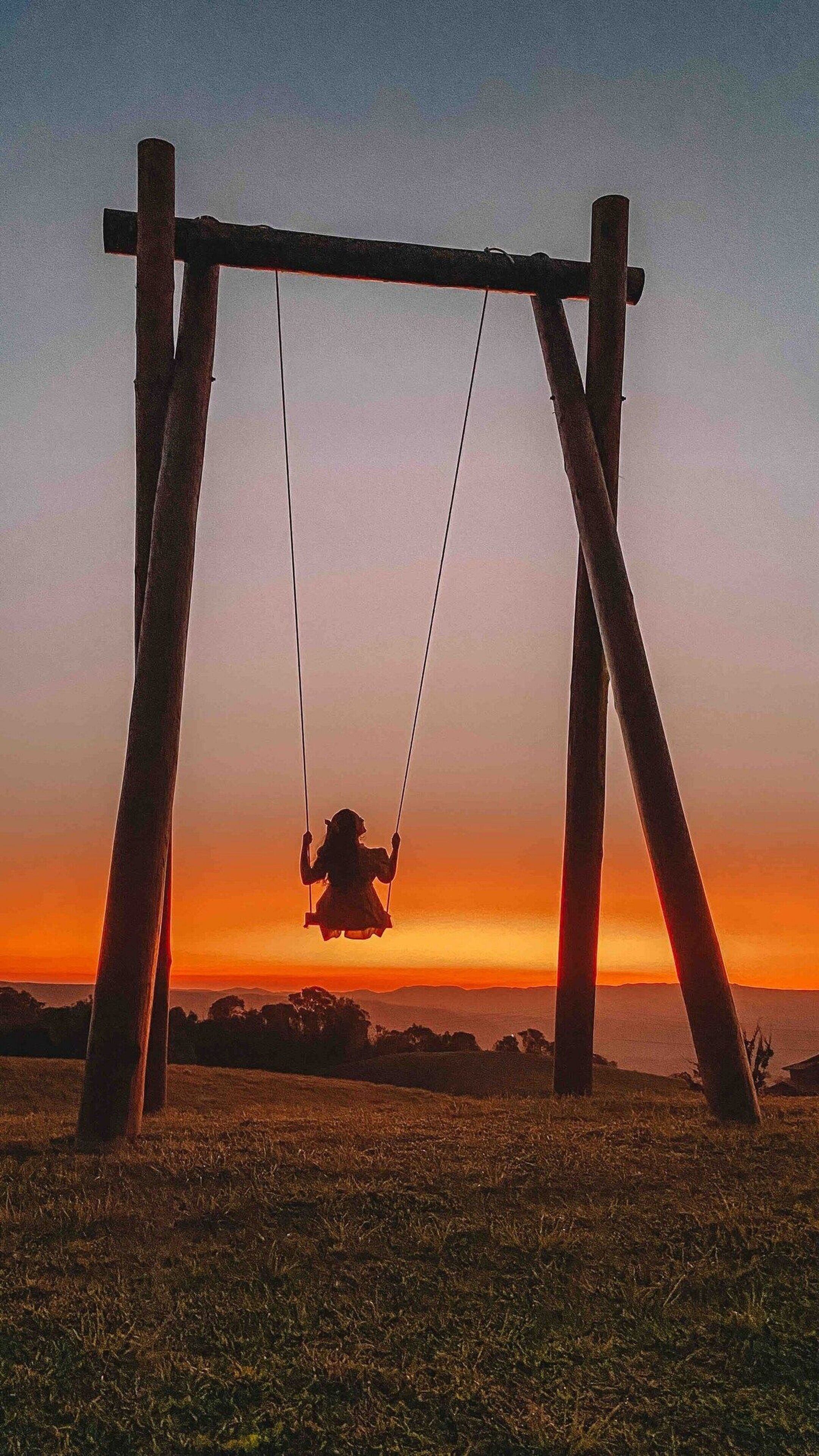 Un columpio en un campo cubierto de hierba, con un atardecer de fondo.
