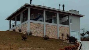A modern two-story house with a stone facade, a covered porch, and a small garden with shrubs.