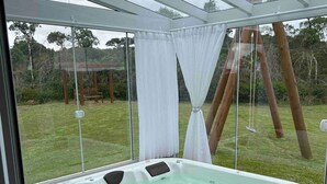 Een hottub met glazen omheining, omringd door een houten terras en een gazon.