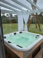 Uma banheira de hidromassagem com estrutura de vidro, rodeada por um deck de madeira e um gramado.