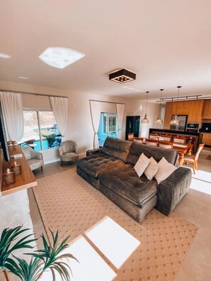A modern living room with a large sectional sofa, a dining area, and a kitchen with wooden cabinets and pendant lighting. - Casa Paraíso do Sol - Rancho Queimado (Rancho Queimado)