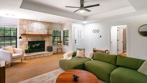 A spacious living room with a stone fireplace, green sofa, and a ceiling fan.