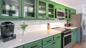 A kitchen with green cabinets, a microwave, a coffee maker, and a refrigerator.