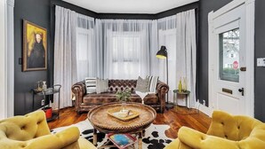 Een woonkamer met een bruine leren bank, twee gele fauteuils, een ronde houten salontafel en een zwarte vloerlamp.