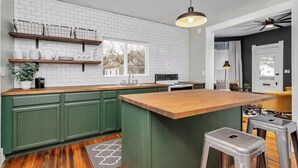 Een keuken met groene kastjes, een houten aanrechtblad en een hangende lamp.