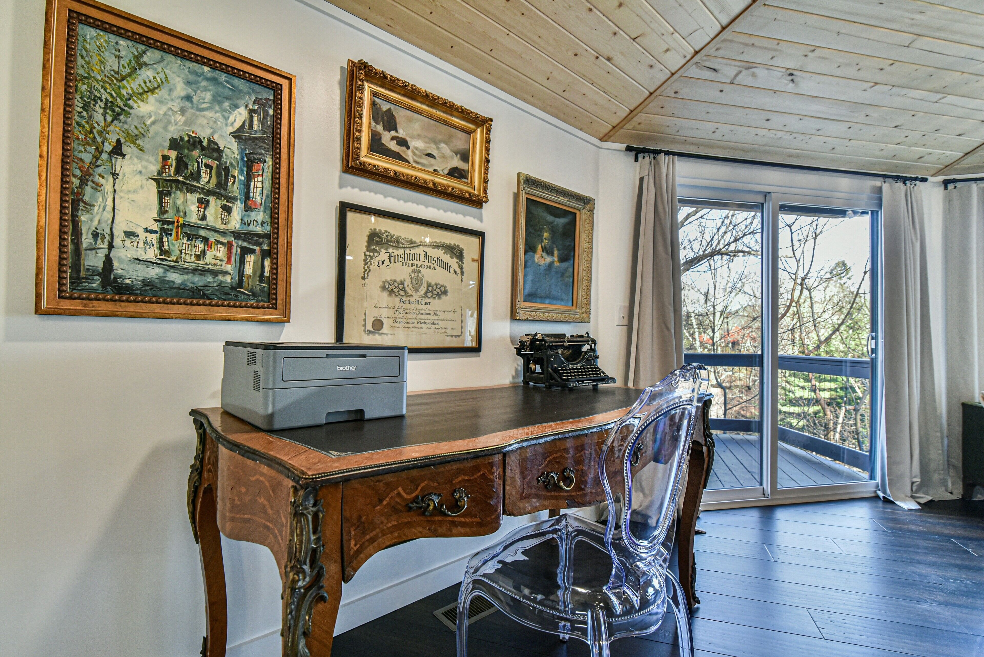 Una habitación con un escritorio de madera, una máquina de escribir antigua y obras de arte enmarcadas en la pared.