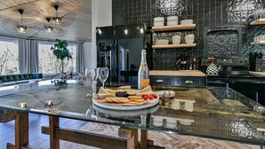 A modern kitchen with a large island, black tiled backsplash, and wooden shelves. - La Maison Mirch - Luxe Design Retreat (Asheville)