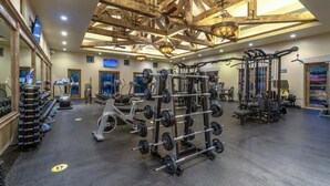 A gym with various exercise equipment, a ceiling with exposed beams, and a large window providing natural light.