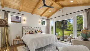 Une chambre spacieuse avec un grand lit, un ventilateur de plafond et une vue sur l’extérieur grâce à de grandes fenêtres.