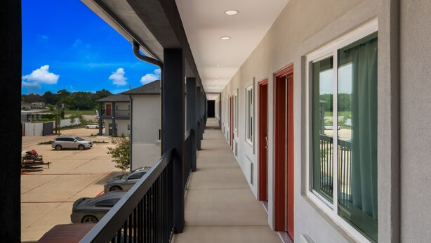 Un long couloir étroit, avec un balcon d’un côté, qui mène à l’entrée d’un immeuble reconnaissable à sa porte rouge.