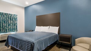 Une chambre d’hôtel moderne avec un grand lit, une table de chevet, une chaise et un grand tableau abstrait accroché au mur.