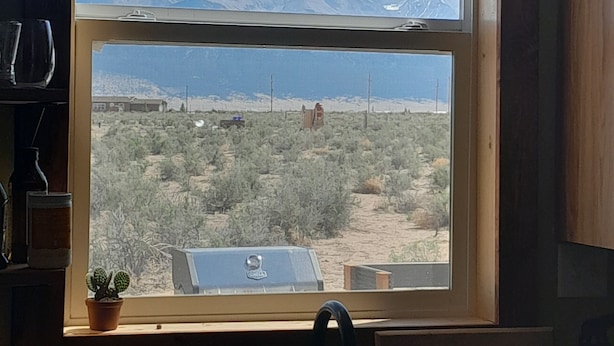 Une fenêtre donnant sur un paysage désertique et des montagnes.