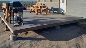 Une cabane avec une terrasse, des tables de pique-nique et un barbecue.