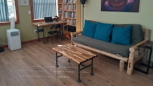 Un salon chaleureux avec un plancher en bois, un canapé agrémenté de coussins bleus, une table basse en bois, une bibliothèque et un tableau accroché au mur.