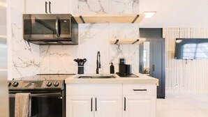 Een moderne keuken met witte kastjes, een ingebouwde magnetron en een koffieapparaat.